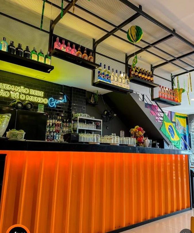 Balcão laranja do Sampa Villa com neon e prateleiras de garrafas